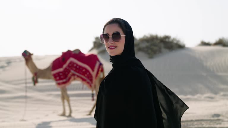 portrait of Muslim woman at the desert with camelleers leading camel behind