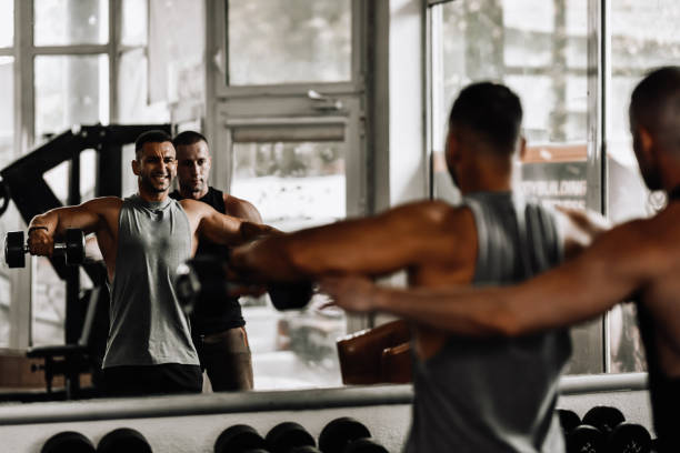 istock Instructor Correcting Male Athlete During Shoulder Exercise In Gym 2004950084