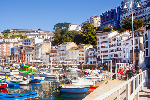 Luarca village and fishing harbour, Asturias, Spain. Multicolored fishing boats, sidewalk cafes and white houses townscape, clear sky  in the background.