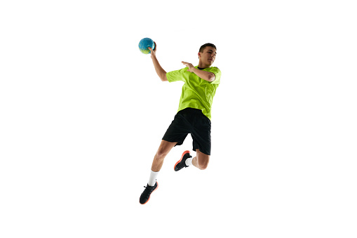 Dynamic image of young man in uniform, handball player in motion during game, practicing, jumping with ball against white studio background. Concept of professional sport, tournament, competition