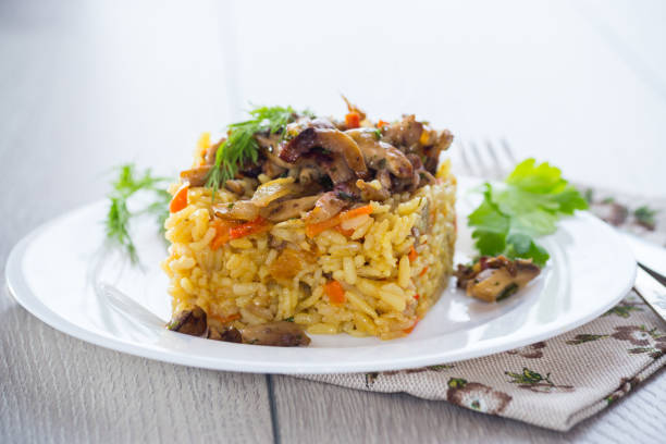 Diet pilaf with mushrooms and vegetables in a plate on a light wooden table. Vegetarian food.