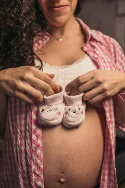 Close-up of Pregnant Woman Holding Pink Baby Booties. Unrecognizable pregnant woman holding pink baby booties near her belly.