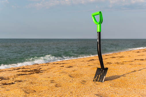 a hiking shovel in the sand, with a bright green handle so as not to lose it. sea beach, hiking camp or off-road travel concept