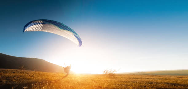 istock A paraglider glides along the ground at sunset with mountains in the background. Panoramic shot banner for paragliding in warm colors. Glare from the sun in the frame 2005014681