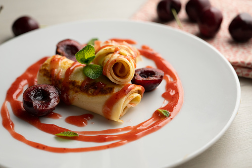 Delicious French crepes with fresh cherries and red fruit syrup..