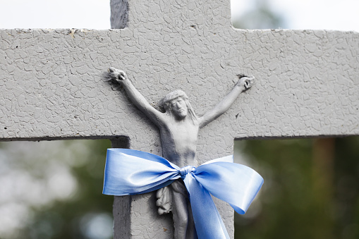 Stone rusty Jesus figure. Blue ribbon. Orthodox cemetery.