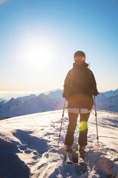szczęśliwa kobieta w kombinezonie narciarskim i kasku stoi w górach na tle pasma górskiego w słoneczny zimowy dzień. chwila odpoczynku, relaksu, przyjemności, ferie zimowe - sunny day mountain mountain range winter zdjęcia i obrazy z banku zdjęć