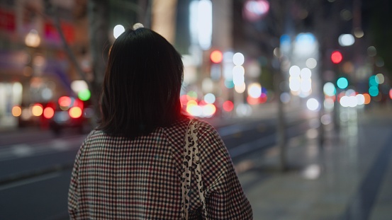 A woman is walking in the city alone at night.