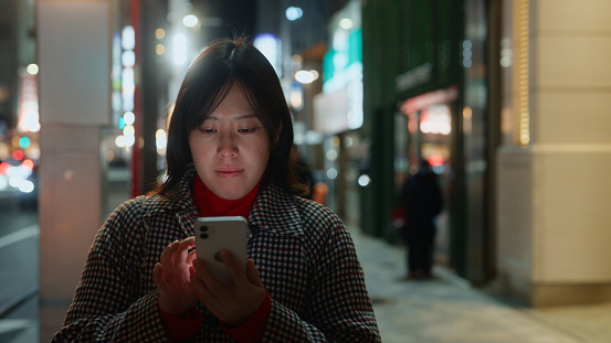 A woman is using her smart phone in the city at night.
