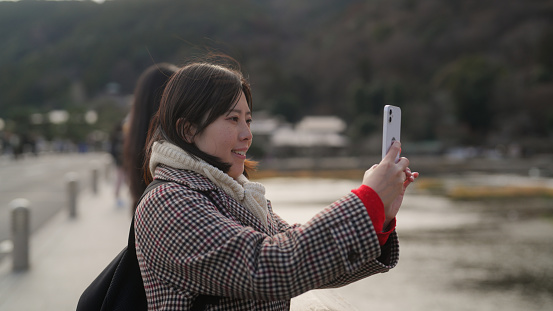 A female tourist is visiting Kyoto and taking photos and videos with her mobile smart phone in Japan.