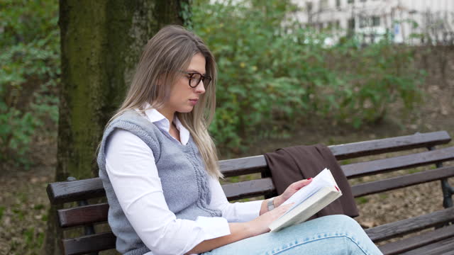 Young businesswoman taking a break from work sitting in the park relaxing while reading a book. Business female office worker read outdoor during lunch break to clear her mind for new job opportunity