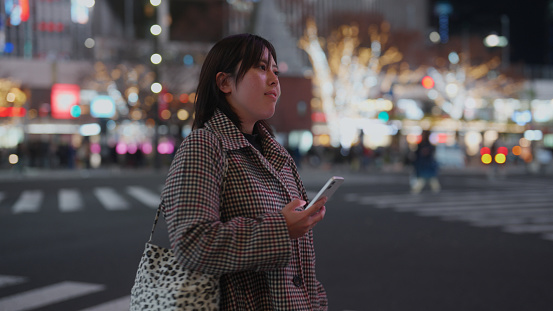 A woman is using her smart phone in the city at night.