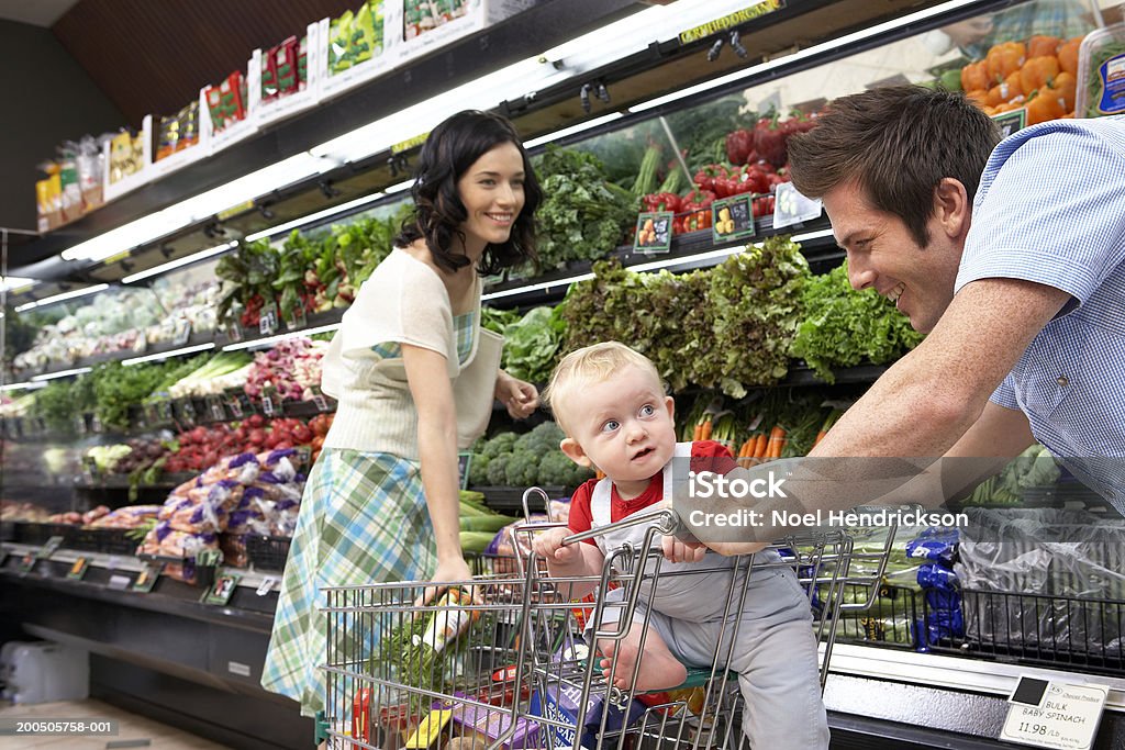 Pareja joven con bebé son (12 a 15 meses) en supermercado, smilin - Foto de stock de Supermercado libre de derechos