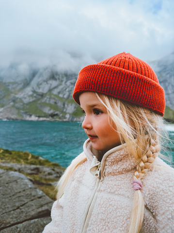 Child girl traveling in Norway family vacations lifestyle outdoor 4 years old kid portrait in red hat and warm fleece jacket