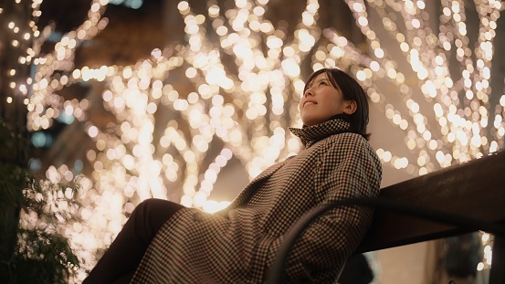 A portrait of an Asian woman sitting under Christmas illumination lights in the city at night.