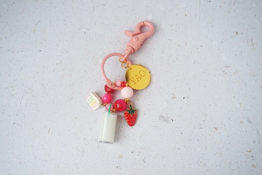 Bottle of milk and strawberry attached to pink key chain on white background. Top view.