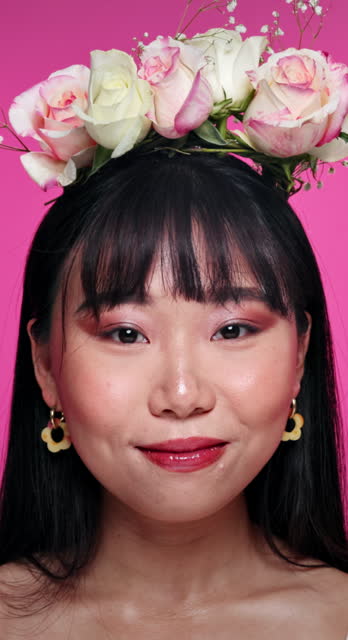 Face, beauty and flowers on hair with asian woman in studio on pink background for natural wellness. Portrait, skincare and floral bouquet with happy young person at spa or salon for facial aesthetic