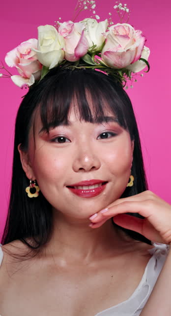Face, beauty and flowers with asian woman at salon in studio on pink background for natural wellness. Portrait, skincare and floral bouquet on hair with happy young person at spa for facial aesthetic
