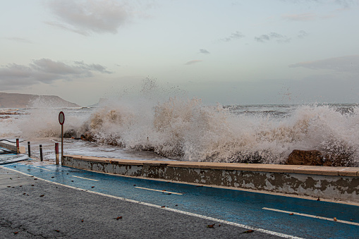 An ocean wave splashing on the road with a parking meter.