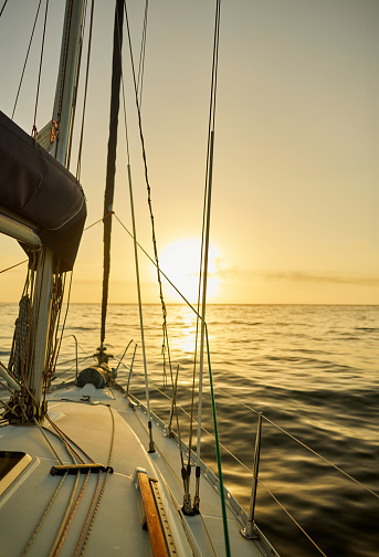 The deck of a yacht basks in the golden glow of the setting sun, painting a picture of tranquility on the water. The rigging and sails stand out against the calm sea, promising a peaceful end to a day of sailing.