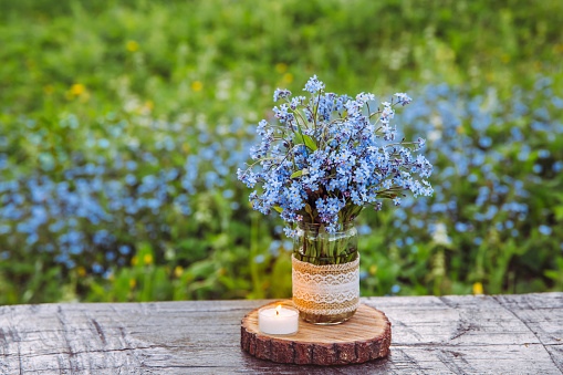 Bouquet of blue blossom wild flowers Myosotis also known as Forget me not or scorpion grasses in decorated mason jar. Beautiful vintage floral still life.