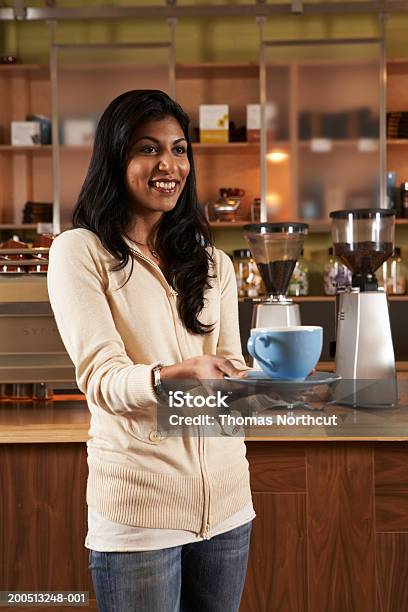 Young Woman Holding Cup Of Coffee In Cafe Looking Away Smiling Stock Photo - Download Image Now