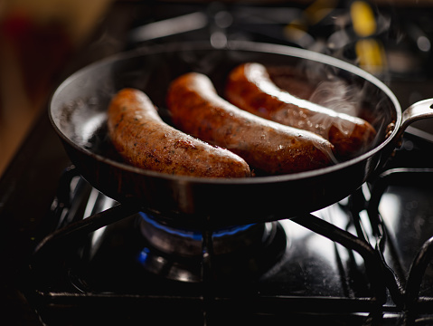 Hot dogs cooking on a stovetop, emitting smoky fumes