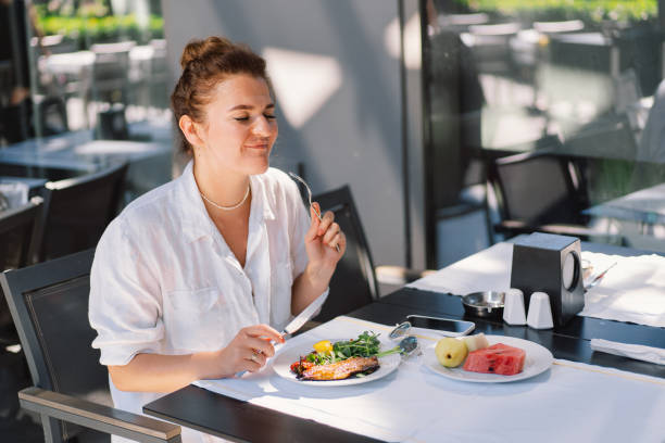 istock A woman in a white shirt eats lunch or breakfast outdoors in a cafe. 2005198169