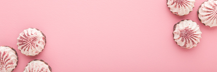 Beautiful white vanilla soft zephyrs with dry strawberry powder on light pink table background. Pastel color. Closeup. Sweet food wide banner. Empty place for text. Top down view.