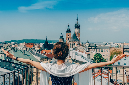 Rear view of woman with hands raised admiring Krakow from rooftop terrace