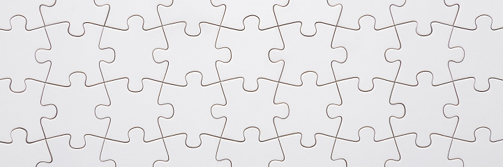 Finished puzzle from different many white pieces. Jigsaw background. Closeup. Wide banner. Empty place for text. Top down view.