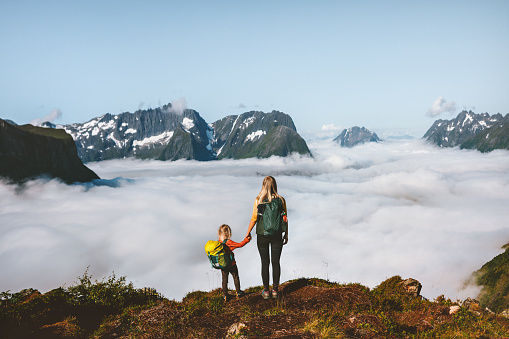 Mother and daughter hiking in Norway mountains, family adventure in the great outdoors. Together on active vacations parent and kid girl with backpack trekking above clouds