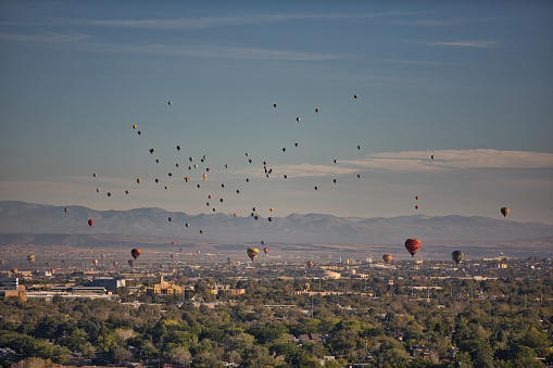 Wide shot of balloons covering the sky over Albuquerque, New Mexico with the Sandia Mountains in the background