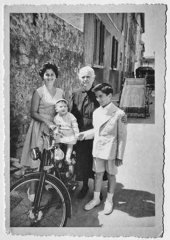 Granmother and nephews with bicycle standing in a street. 1956.