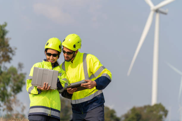 istock Harnessing Clean Energy Innovation. Engineers gather at a wind farm, passionately discussing the future of clean energy. The group, adorned in safety suits and reflective clothing, engages in a conversation while examining crucial data on their laptop. 2005329643