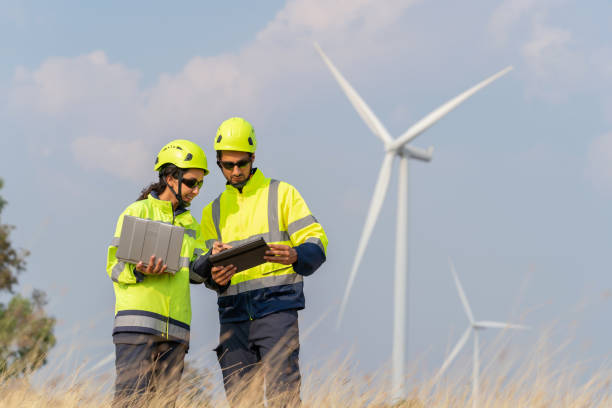 istock Guides Colleague through Wind Farm Excellence.  Engineer in protective clothing walking through a wind farm, pointing out a wind turbine to a colleague. Renewable energy and environmental conservation 2005329652