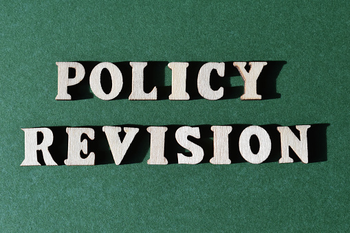 Policy Revision, words in wooden alphabet letters isolated on green background as banner headline