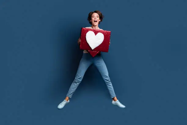 Photo of Full length photo of lovely young lady excited jump hold heart icon dressed white garment isolated on dark blue color background