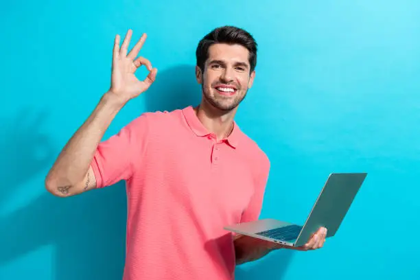 Photo of Photo of young guy pink t shirt demonstrate okey sign feedback about new macbook processor productivity isolated on cyan color background