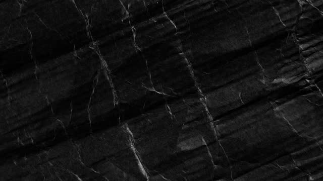 Crumpled black paper with wrinkles and folds. Dark cardboard abstract background. Rotation