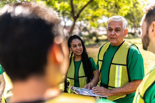 Senior recycler man giving instructions to volunteers on public park