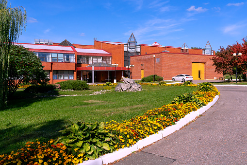17.09.2023, Russia, Moscow region, Stupino city district, Petrovo village, the territory of the Zarya Boarding House. The gym building was photographed against the blue sky. In the foreground there is a green lawn with decorative flower beds and a stone installation.