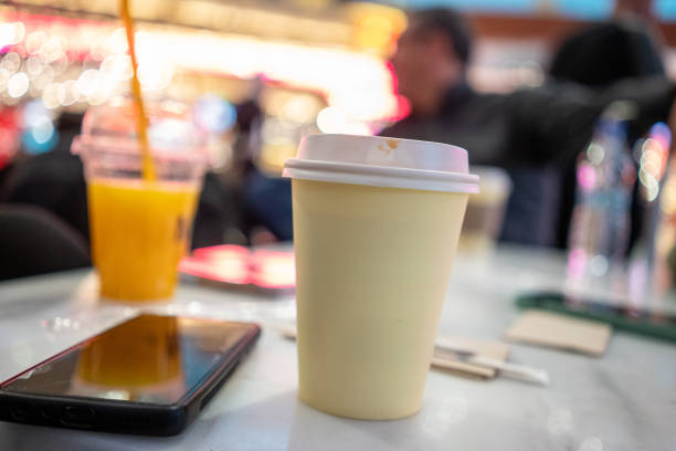 take a way coffee cuup and smarthphone are foreground focus on foreground people are background at cafe horizontal food and drink still
