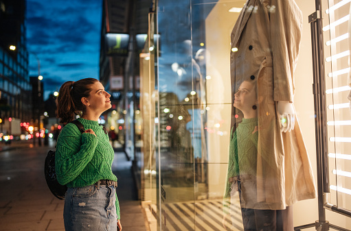 Young woman looking at store display at night in the city.