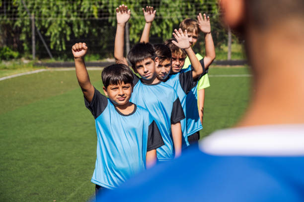 Enthusiastic group of young soccer players with coach during a practice session on outdoor field.