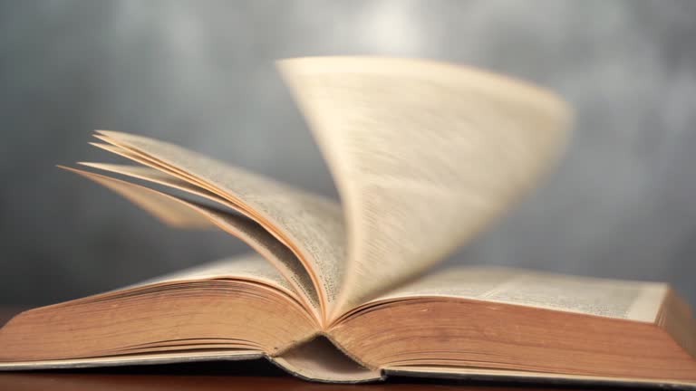 Books on a table. A gentle breeze is blowing through the pages of the books, causing them to turn one by one, causing the pages of the top book to turn slowly.