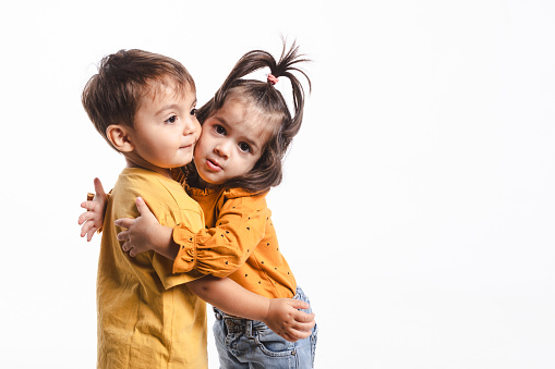 A two-year-old boy and girl hugging on white background