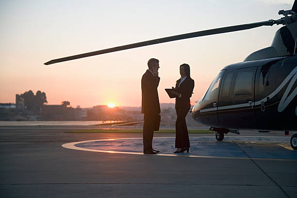 silhouette of businessman and woman standing by helicopter, side view - helipad foto e immagini stock