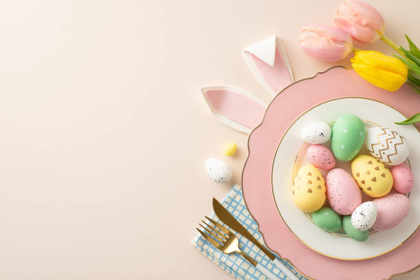 istock Easter feast table setting concept. Overhead  shot showcasing plate of vibrant eggs, rabbit ears, utensils, and elegant tulips on a soft beige backdrop, leaving space for text 2005515018
