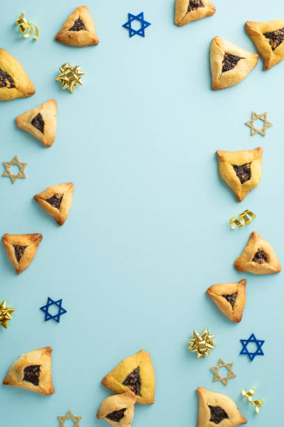 istock Festive Purim spread. Vertical top view featuring triangular cookies, Star of David motifs, and gold ribbon stars on a soft blue surface, with space for wording 2005515595